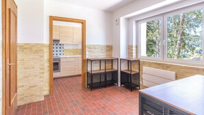 A kitchen with a brick floor, wooden cabinets, a window with a view of trees, and a radiator.