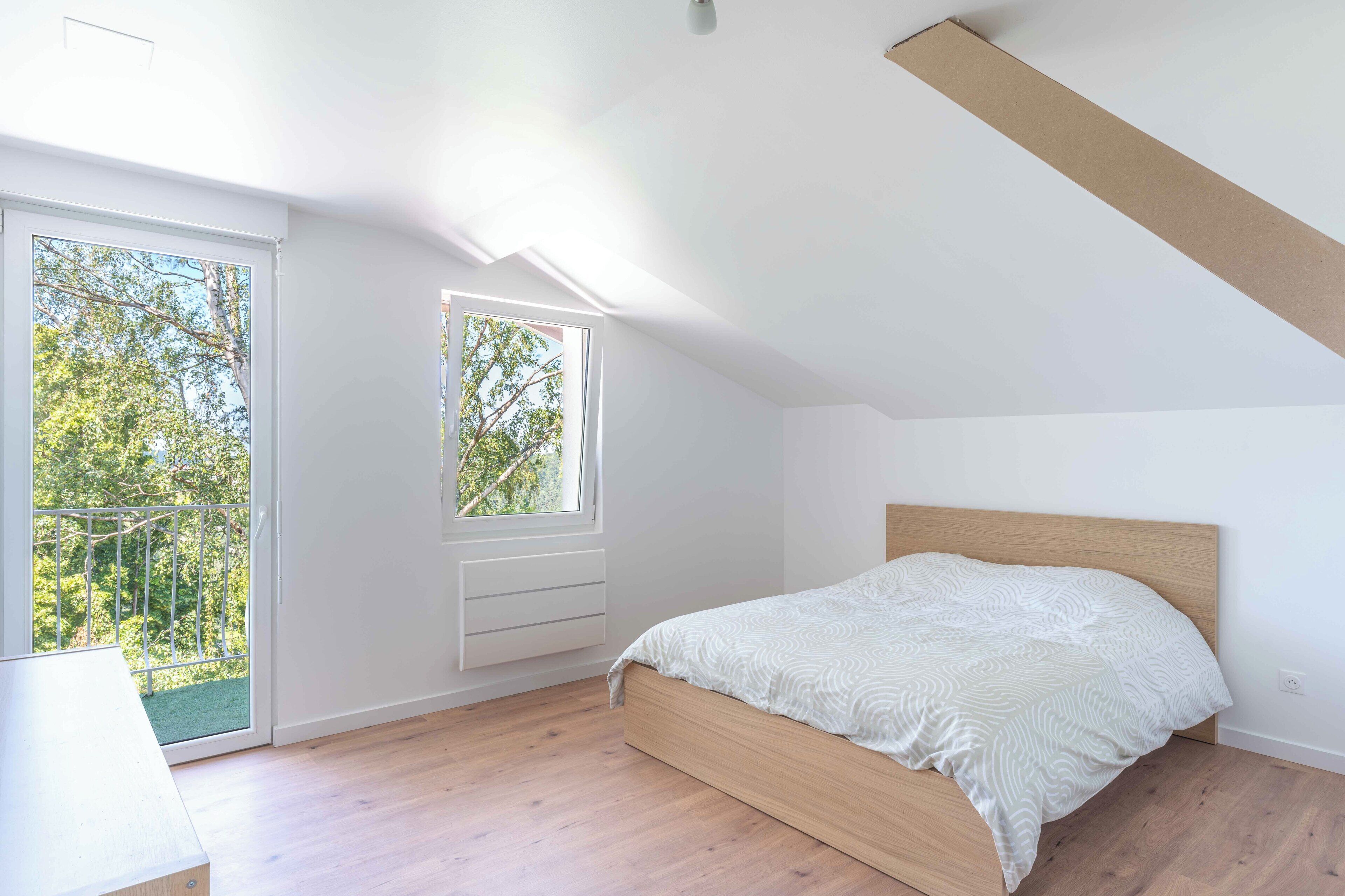 A bedroom with a wooden bed, a large window, and a balcony.