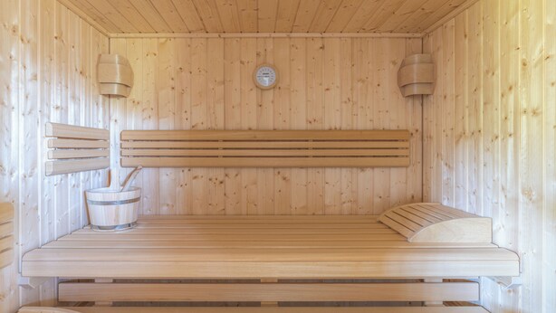 A wooden sauna with benches, a wall-mounted heater, and a thermometer.