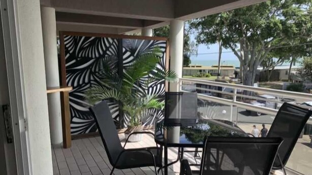 Ein Balkon mit Glastisch und Stühlen, Blick aufs Meer und einer Wand mit tropischen Pflanzen.
