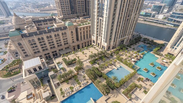Un hotel de gran altura con múltiples piscinas, un patio con palmeras y vistas a la ciudad.