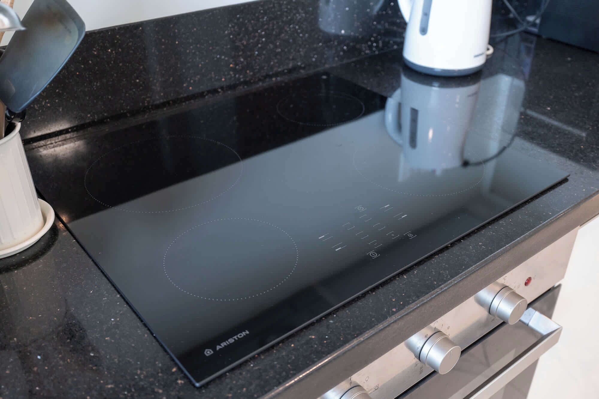 Una cocina de inducción negra con un panel de control y una tetera sobre una encimera.