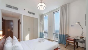 Habitación de hotel con cama, escritorio, silla y ventanas amplias con vista a la ciudad.