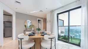 A modern dining area with a round table, four chairs, and a large window offering a city view. - StayShort-Elegant 1 Bedroom City View Apartment Square Tower JVC (Dubai)