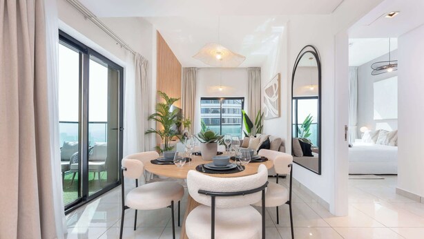 A modern dining area with a round table, white chairs, and a large window with curtains. - StayShort-Elegant 1 Bedroom City View Apartment Square Tower JVC (Dubai)