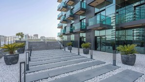 A modern building with a glass facade, outdoor steps leading to a balcony, and potted plants along the pathway. - StayShort-Elegant 1 Bedroom City View Apartment Square Tower JVC (Dubai)