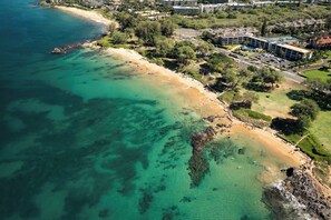 An aerial view of a coastal area with a beach, buildings, and a road.