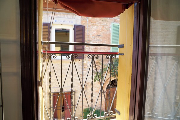 A wrought iron balcony gate with a red awning, a wooden door, and a brick building in the background.