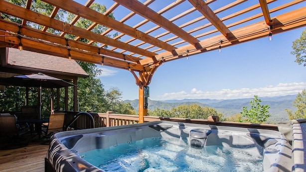 Un bain à remous sous une pergola en bois, avec vue sur les montagnes.