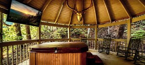 A wooden gazebo with a hot tub, wooden benches, and a mounted deer skull.