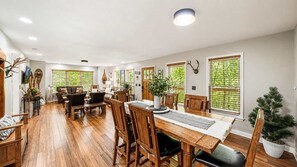 Een ruime eethoek met een houten tafel en stoelen, omringd door grote ramen met zonwering.