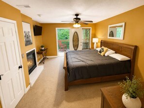 A bedroom with a bed, a ceiling fan, a fireplace, a door, and a window.