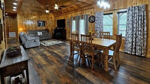 L’intérieur chaleureux d’un chalet avec un plafond en bois, un canapé, une table à manger avec des chaises et une cheminée.