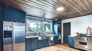 Een moderne keuken met roestvrijstalen apparatuur, donkere kastjes en een houten plafond.