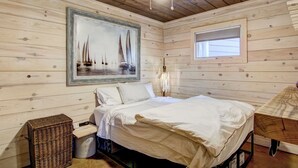 Een houten kamer met een bed, een lijst met een schilderij, een raam en een plafondventilator.