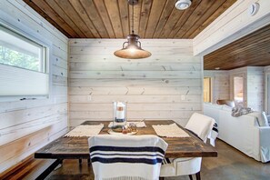 Un interior de madera con una mesa de comedor, sillas, una lámpara colgante y un sofá blanco.