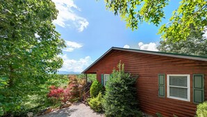 A wooden cabin with a gravel driveway, surrounded by lush greenery and trees. - Sunsets and Moonshine Log Cabin with Outstanding Mountain Views (Bryson City)