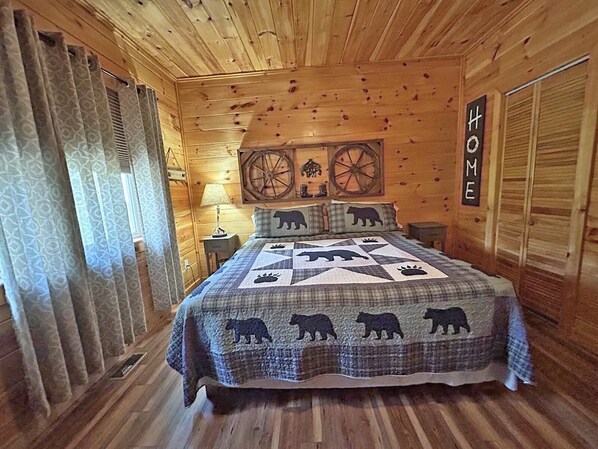 A cozy wooden cabin bedroom with a bed, a nightstand, a lamp, and a 'HOME' sign on the wall.