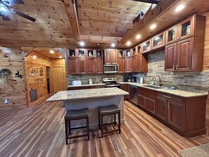 A spacious kitchen with wooden cabinets, granite countertops, and a central island with stools.