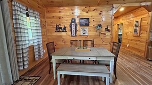 A wooden cabin interior with a dining table, chairs, and a bench.
