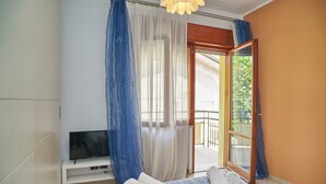 Ein Schlafzimmer mit Bett, Fernseher auf einem Schrank, einem Balkon mit Glastür und Vorhängen.