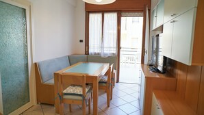 Ein gemütlicher Wohnbereich mit Esstisch, Stühlen, einer Couch, einer Küchenzeile und einer Glastür zum Balkon.