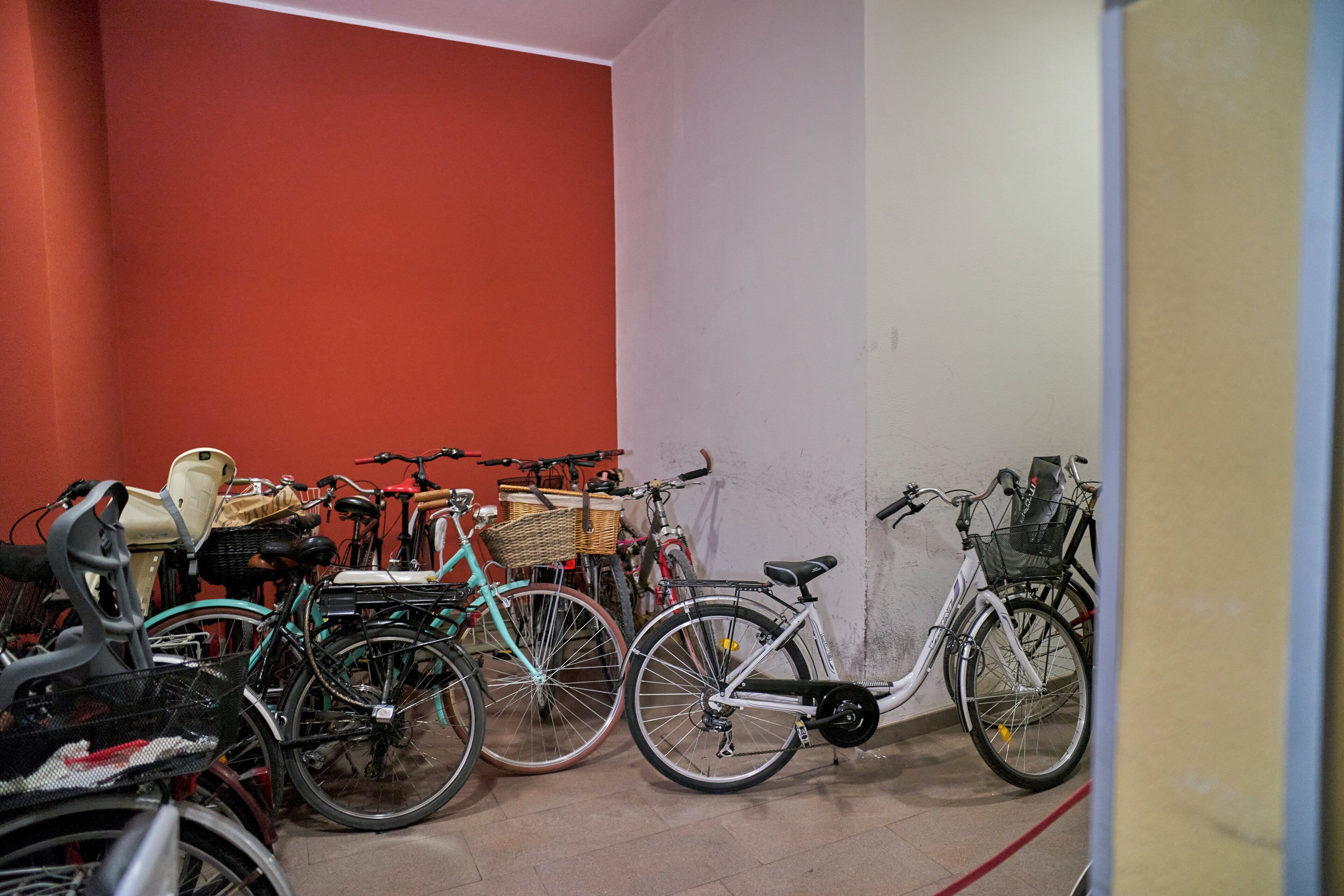 Un espace de stockage pour vélos où sont entreposés plusieurs vélos, dont un vélo blanc avec un panier et un vélo de couleur turquoise.