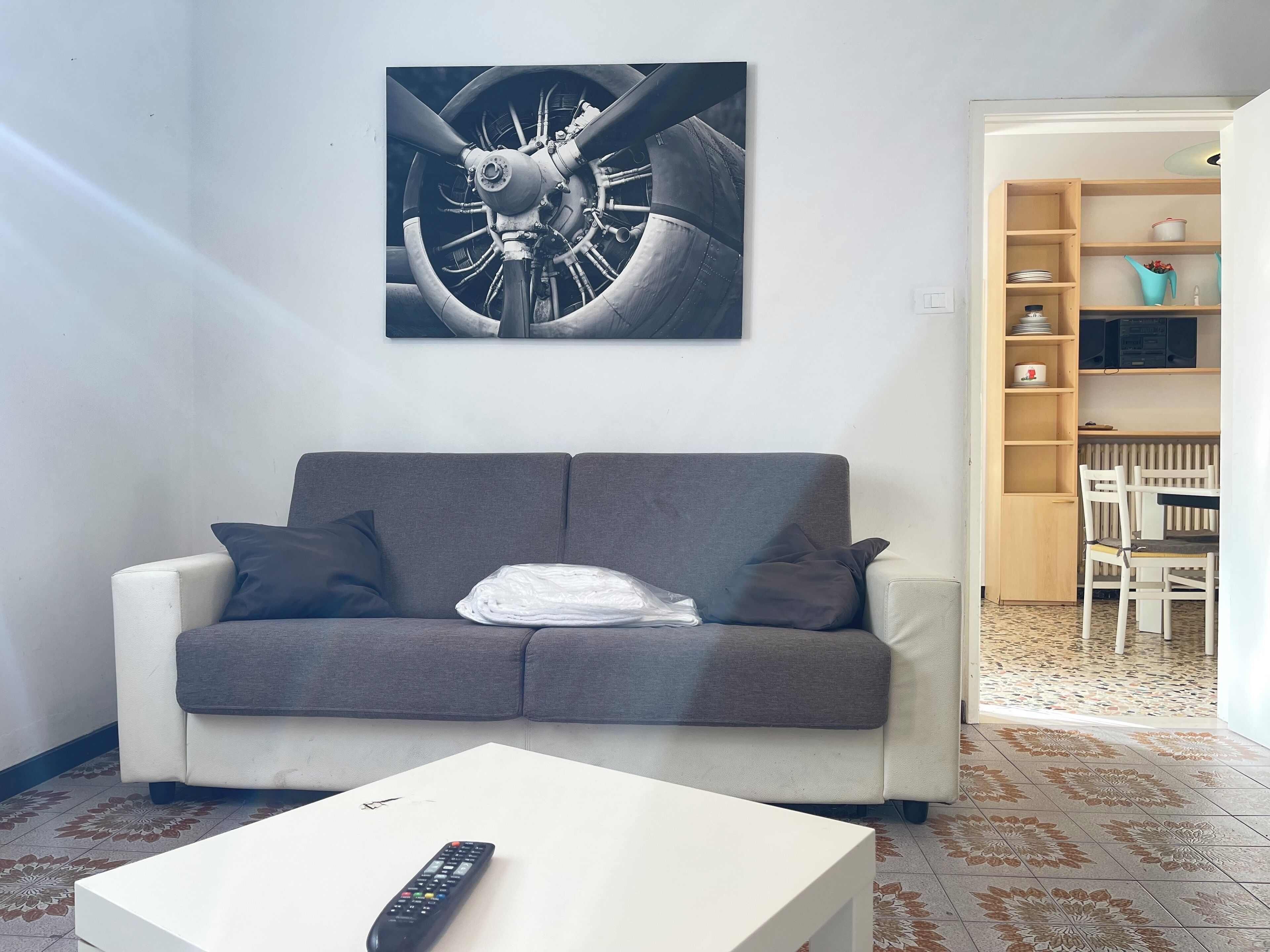 Un soggiorno con un divano grigio, un tavolino da caffè bianco e un telecomando sopra. Sopra il divano, un'opera d'arte a parete.