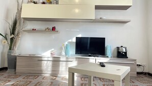A modern living room with a flat-screen TV, a coffee machine, and decorative items on shelves.