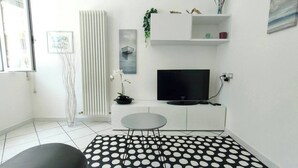 A modern living room with a flat-screen TV, a small round table, and a black and white polka dot rug.
