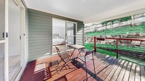 A modern bedroom with a sliding door leading to a balcony. The balcony has a wooden deck and a metal railing.