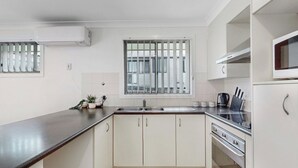 A kitchen with white cabinets, a black countertop, a stainless steel sink, a window with vertical blinds, and a microwave above the oven.