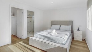 A modern bedroom with a large bed, a walk-in closet, and a shower.