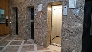 Un ascenseur situé dans un hall d’entrée aux murs de marbre et au sol recouvert de carreaux aux motifs géométriques.