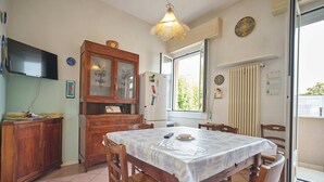 Un comedor con una mesa, sillas, un armario de madera, un televisor y un ventanal con cortinas.