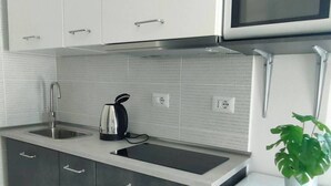 Een moderne keuken met witte kastjes, een roestvrijstalen spoelbak, een waterkoker, een magnetron en een kleine koelkast.