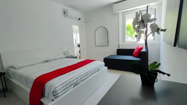 Een moderne slaapkamer met een bed, een bank, een spiegel en een raam met uitzicht op groen.