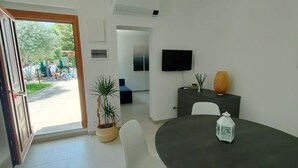 Een moderne kamer met een eettafel, stoelen, een televisie, een potplant en een decoratieve vaas.