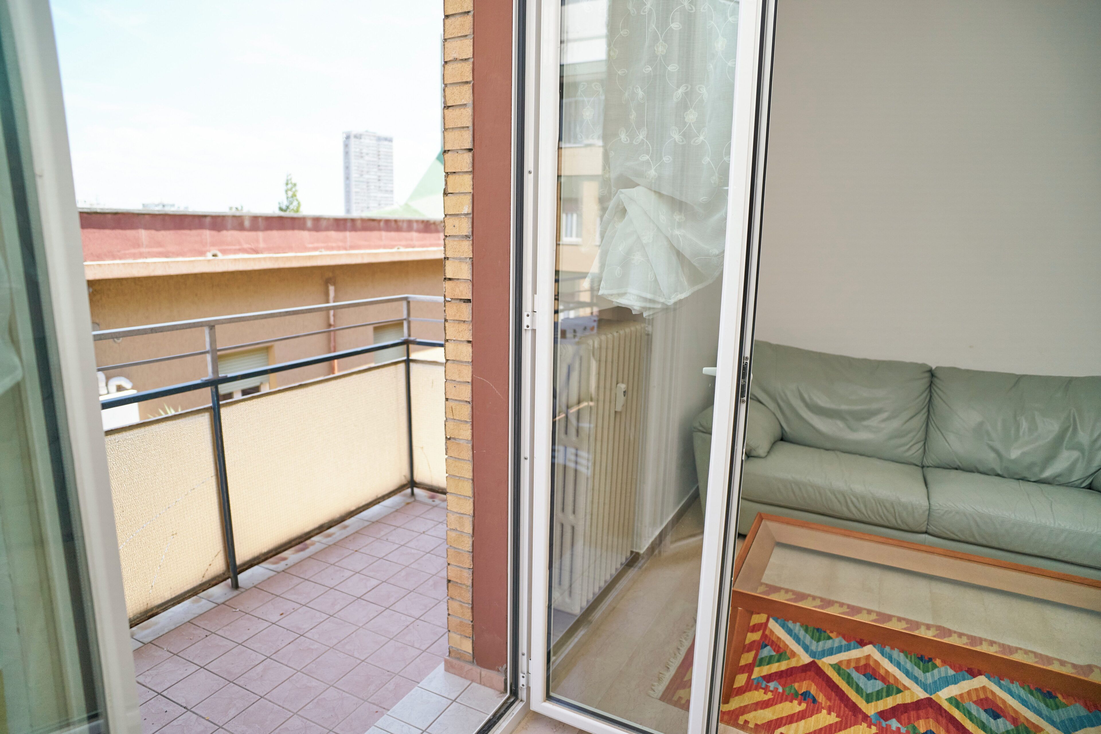 A balcony with a tiled floor, a metal railing, and a view of buildings in the distance.