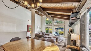 A spacious living area with a large wooden dining table, comfortable seating, and a view of the outdoors through large windows.
