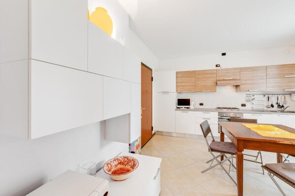 A modern kitchen with white cabinets, a wooden dining table, and a TV.