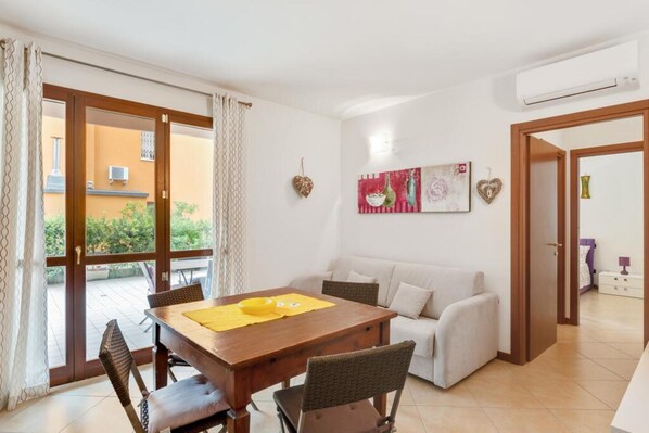A dining area with a wooden table and chairs, a white sofa, and a sliding glass door leading to an outdoor patio.