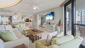 Un salón espacioso con televisor grande, asientos cómodos y un balcón con vistas.