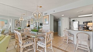 Amplia sala de estar con una mesa de comedor de vidrio rodeada de sillas de mimbre, una cocina con armarios blancos y una lámpara moderna.