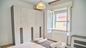 A hotel room with a large bed, a wardrobe, a window with curtains, and a bedside table. - Casa Renata - Three Bedroom Apartment, Sleeps 5 (Rimini)