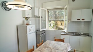 A compact kitchen with white cabinets, a dining table with a patterned tablecloth, a built-in oven, and a window providing a view of the outside. - Casa Renata - Three Bedroom Apartment, Sleeps 5 (Rimini)