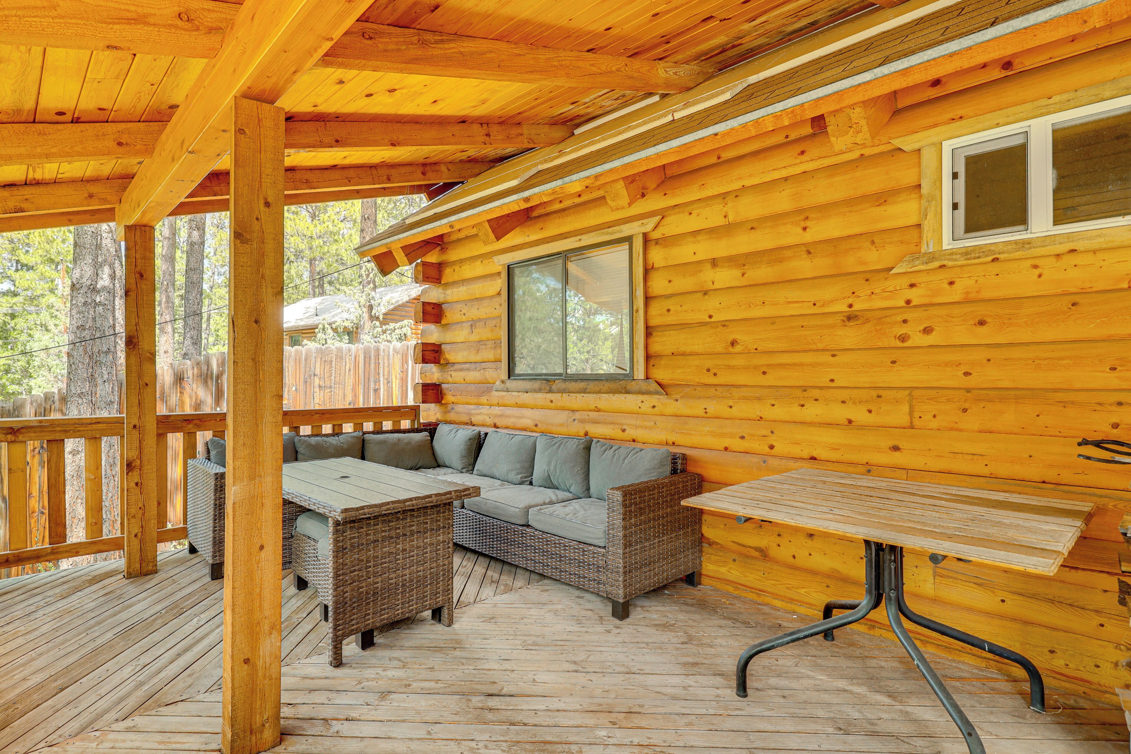 Une terrasse en bois avec un canapé et une table, entourée d’une clôture en bois et d’arbres.