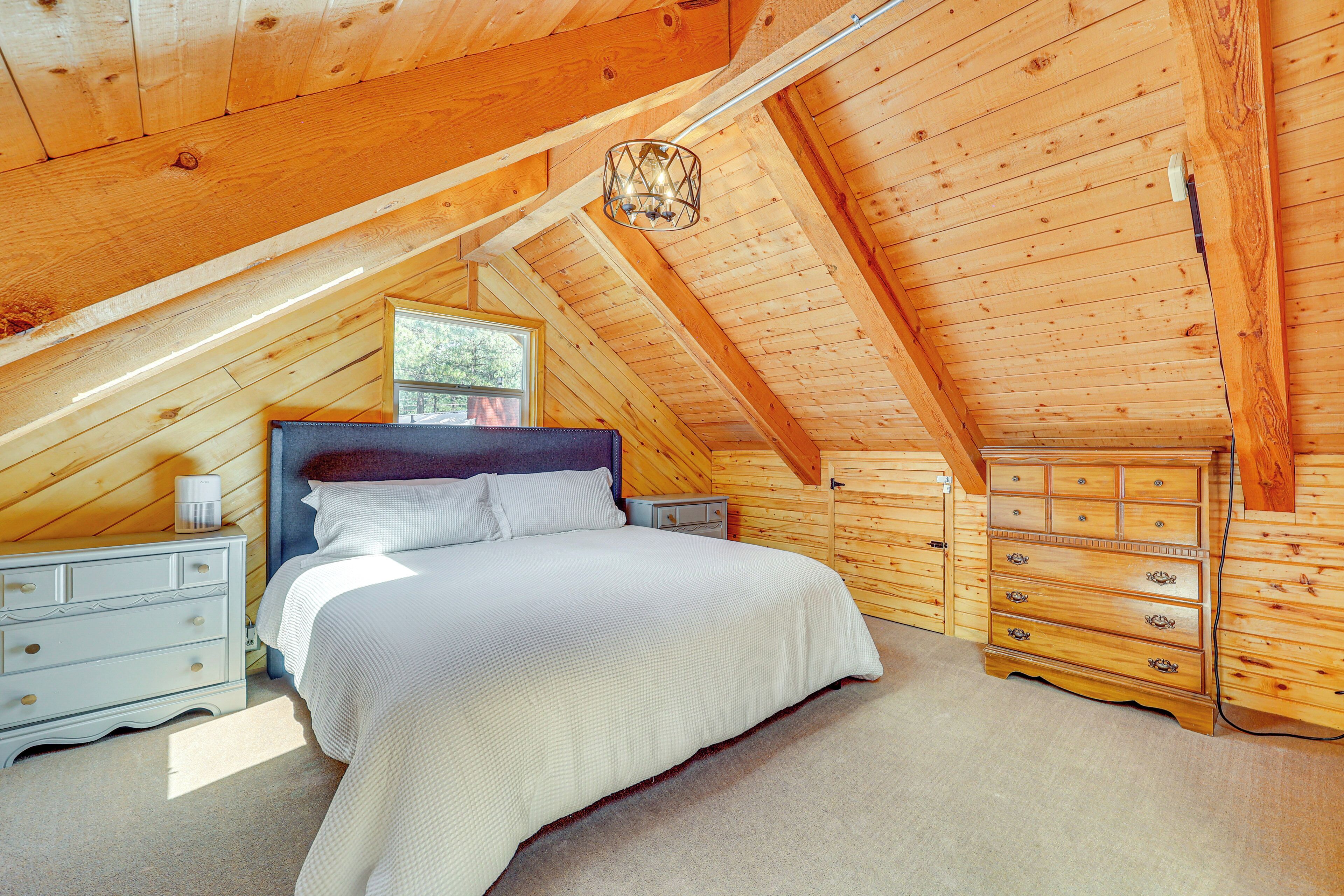 A bedroom with a wooden ceiling, a bed with white bedding, a dresser, and a nightstand.