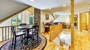 A spacious living area with a round table and chairs, a stone accent wall, and a wooden staircase. - Deck & Mtn Views: Log Cabin By Snowshoe Mountain! (Slaty Fork)