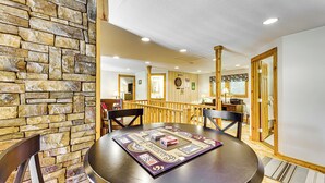 A dining area with a round table, chairs, and a board game. There is a stone wall and wooden flooring. - Deck & Mtn Views: Log Cabin By Snowshoe Mountain! (Slaty Fork)